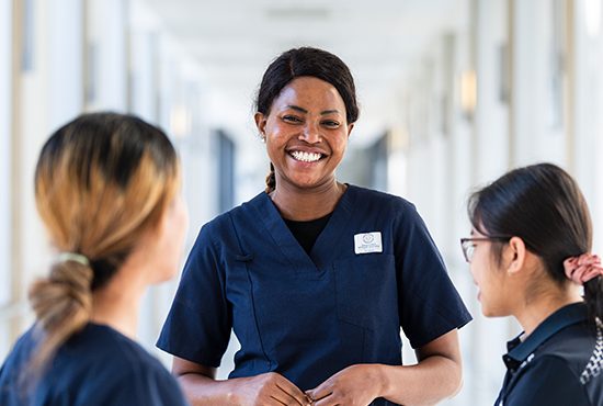 Group of nurses in dark blue scrubs, one smiles to camera