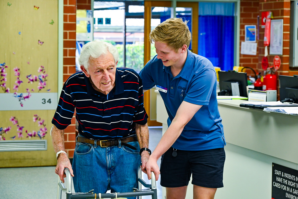 elderly male patient in a walking frame being assisted by a smiling male nurse